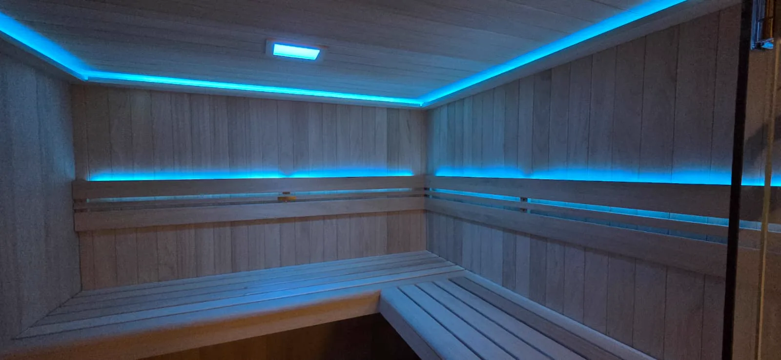De houten banken in de sauna van Topbody Fitness, met blauwe sfeerverlichting langs plafond en rugleuning